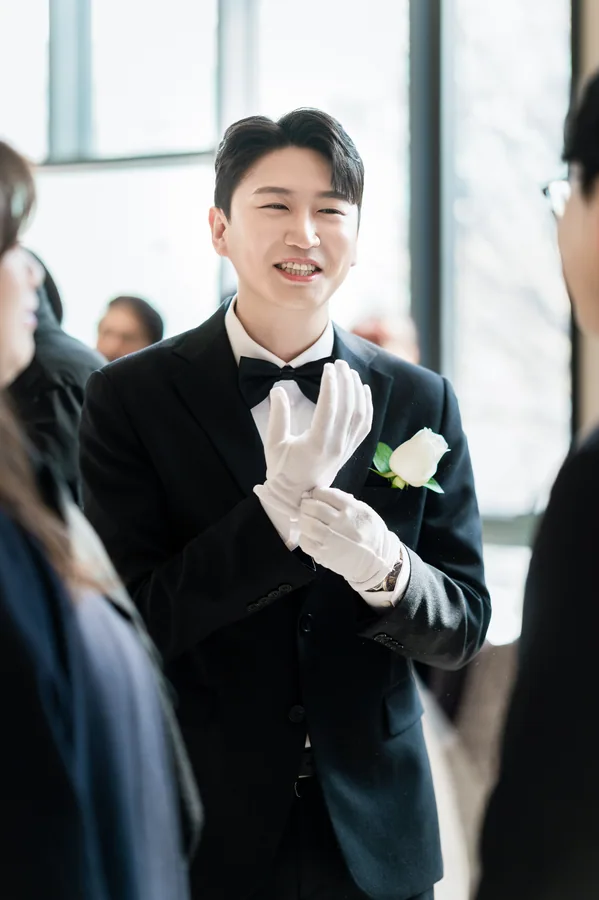 하얀 장갑을 낀 신랑이 하객들 사이에서 미소 짓는 모습