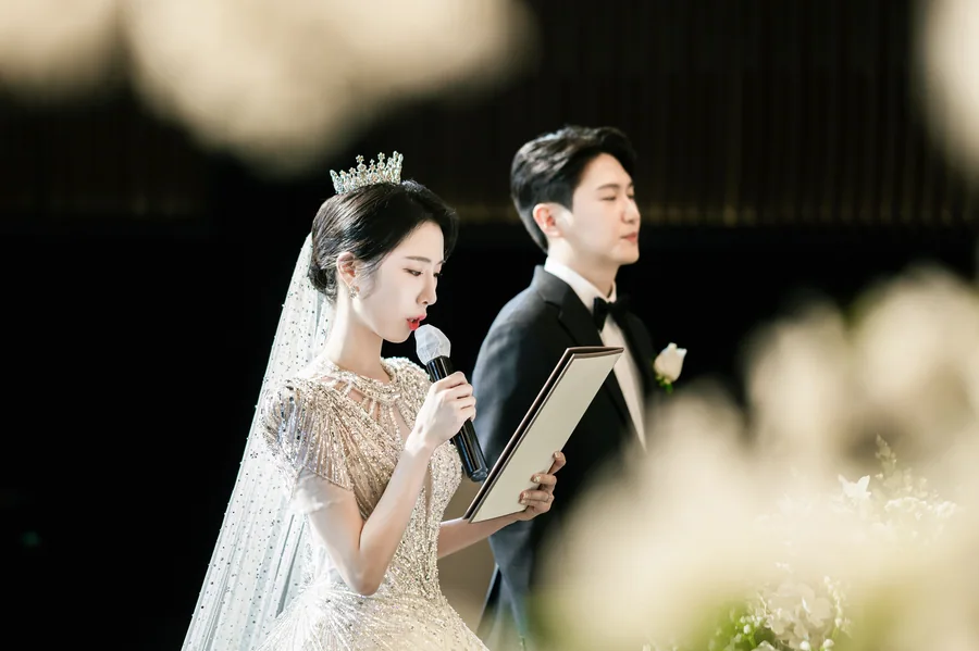 부케 너머로 성혼 서약을 낭독하는 신부와 옆에 선 신랑