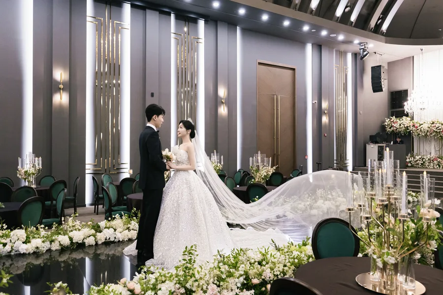 골드 조명 배경, 베일 자락이 옆으로 흩날리는 신랑신부 옆모습 원경