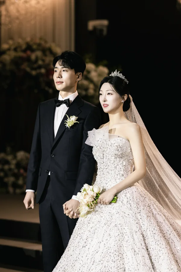 따뜻한 조명 속 손을 맞잡고 나란히 걷는 신랑신부 옆모습